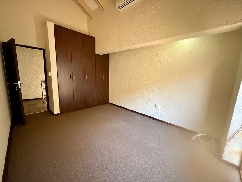 An empty bedroom featuring built-in cupboards, carpeted flooring, a vaulted ceiling, and an installed air conditioning unit.
