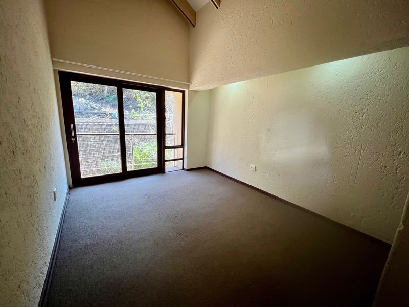 An empty bedroom featuring a high vaulted ceiling, textured walls, carpeted flooring, and a sliding glass door providing access to an outdoor area.