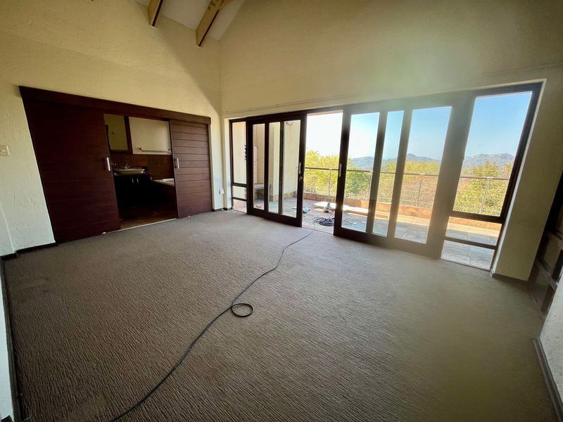 Spacious bedroom featuring a vaulted ceiling, carpeted flooring, and large sliding glass doors opening onto a balcony with scenic views.