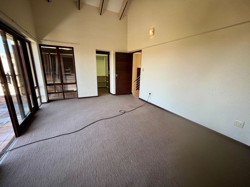 Spacious bedroom featuring a vaulted ceiling with exposed timber beams, carpeted flooring, and direct access to an outdoor area via sliding glass doors.