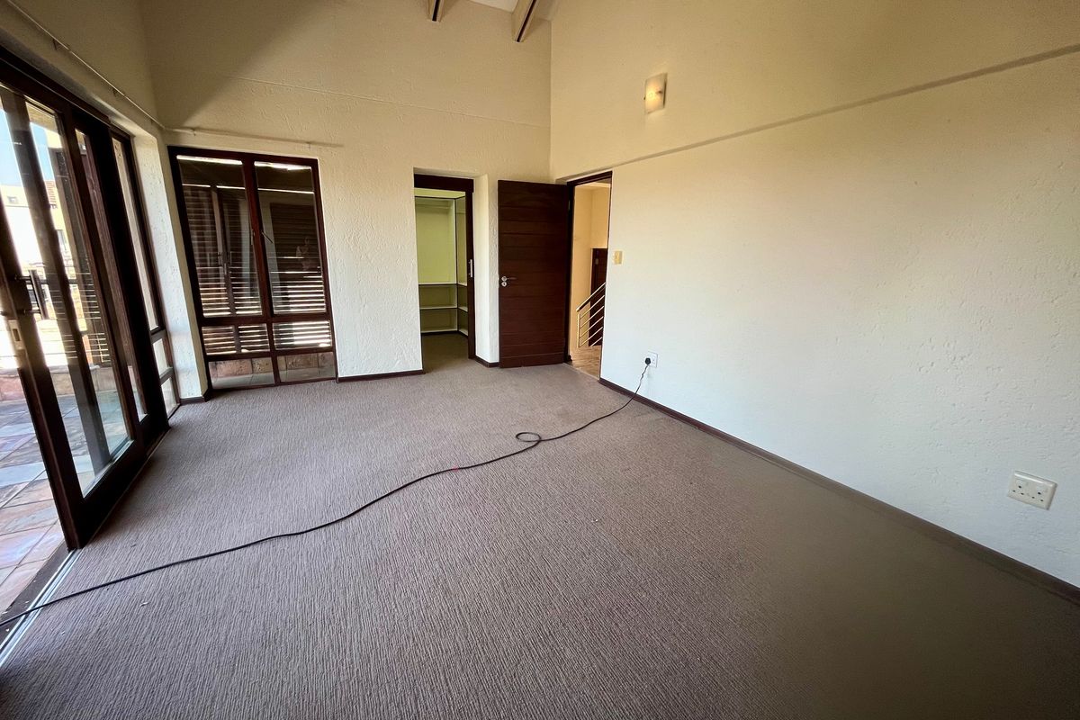 Spacious bedroom featuring a vaulted ceiling with exposed timber beams, carpeted flooring, and direct access to an outdoor area via sliding glass doors.