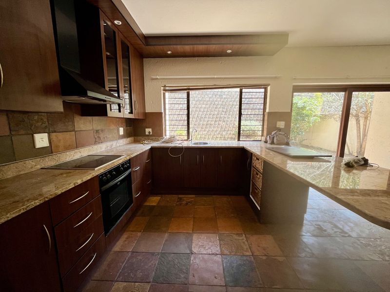 A functional kitchen featuring dark wood cabinetry, granite countertops, built-in appliances, and stone tile flooring with direct access to the outdoor area.
