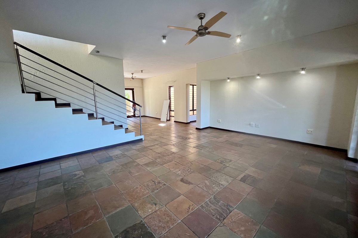 Spacious open-plan living area featuring natural stone tile flooring, a modern staircase with stainless steel balustrade, and integrated ceiling lighting.