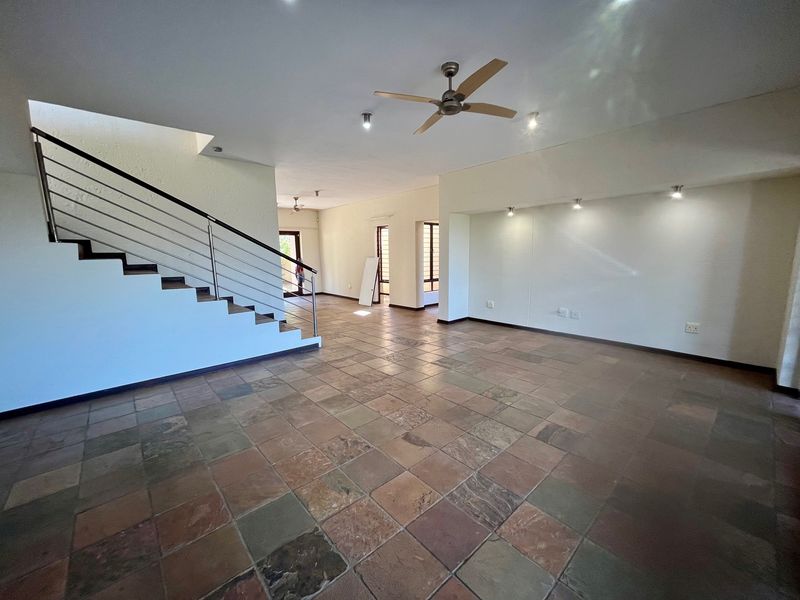 Spacious open-plan living area featuring natural stone tile flooring, a modern staircase with stainless steel balustrade, and integrated ceiling lighting.