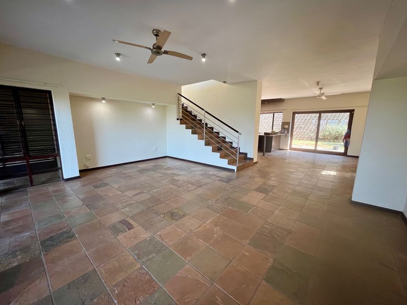 Spacious open-plan living area featuring natural stone tile flooring, a central staircase with metal balustrades, and direct access to the rear garden.