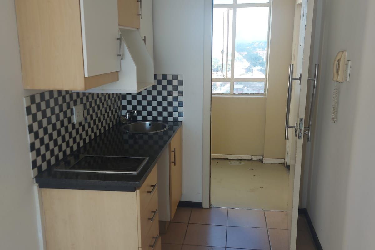 Compact kitchen featuring built-in cabinetry, laminate countertops, and a tiled backsplash, leading to an adjacent balcony area.