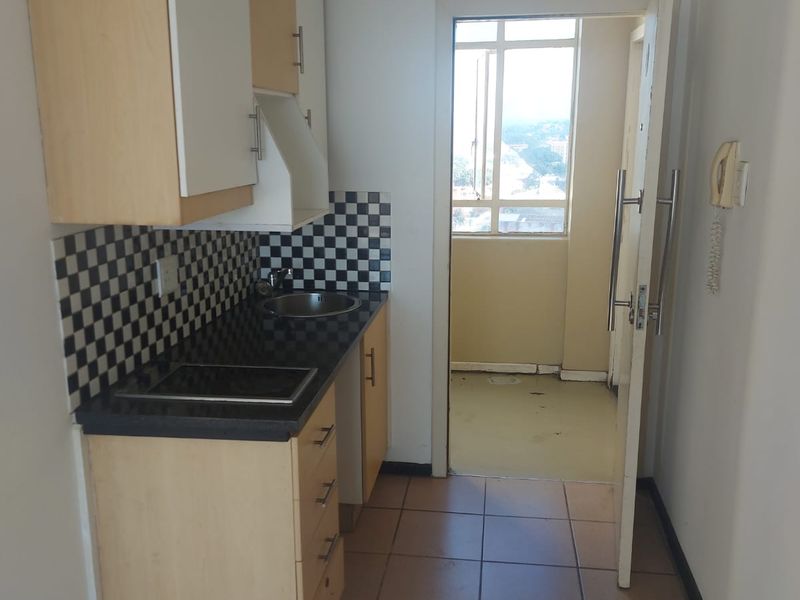 Compact kitchen featuring built-in cabinetry, laminate countertops, and a tiled backsplash, leading to an adjacent balcony area.