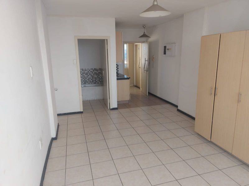 An open-plan living area featuring tiled flooring, built-in storage cupboards, and direct access to the kitchen and bathroom areas.
