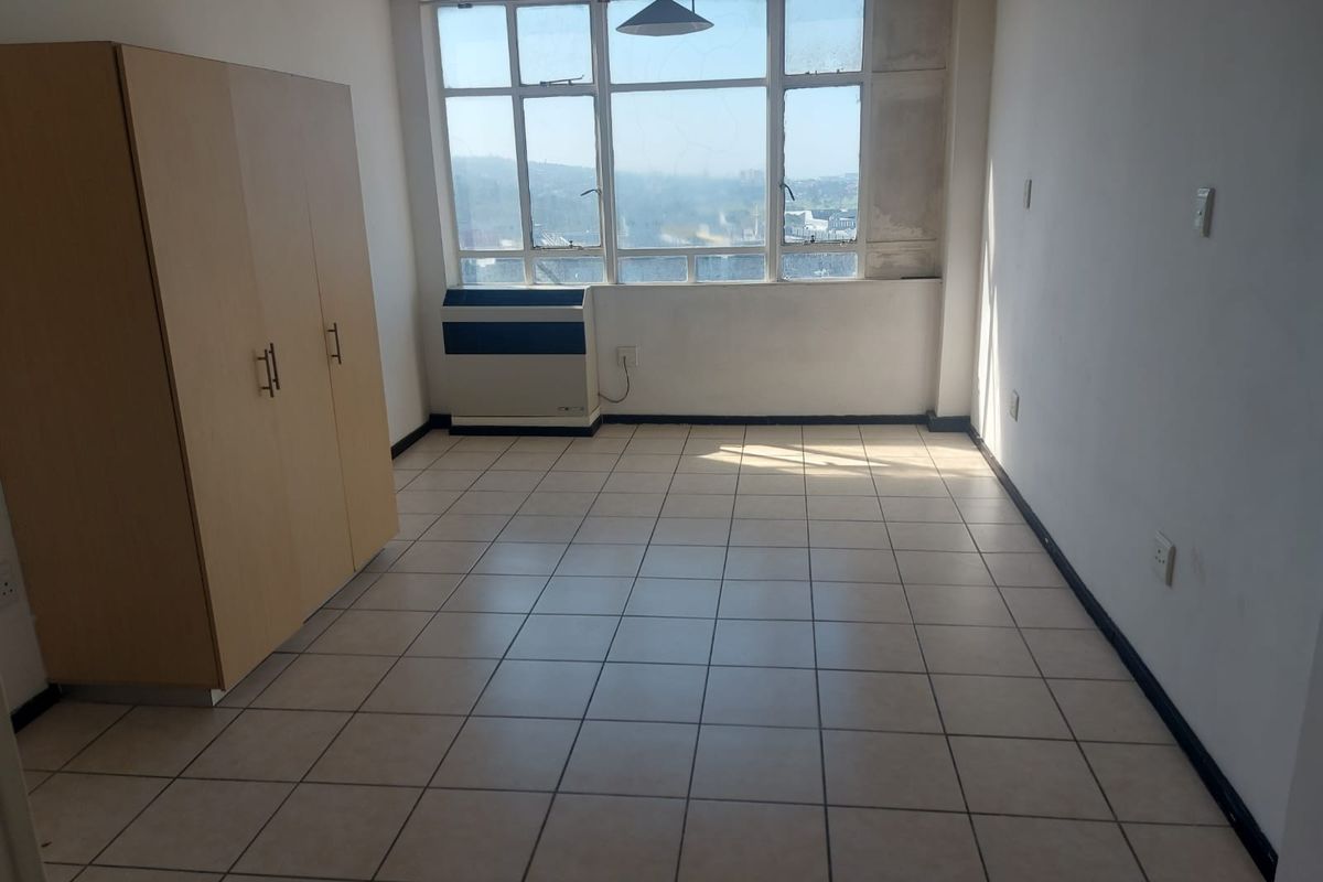 A bedroom featuring tiled flooring, a large window with natural light, and a built-in air conditioning unit.