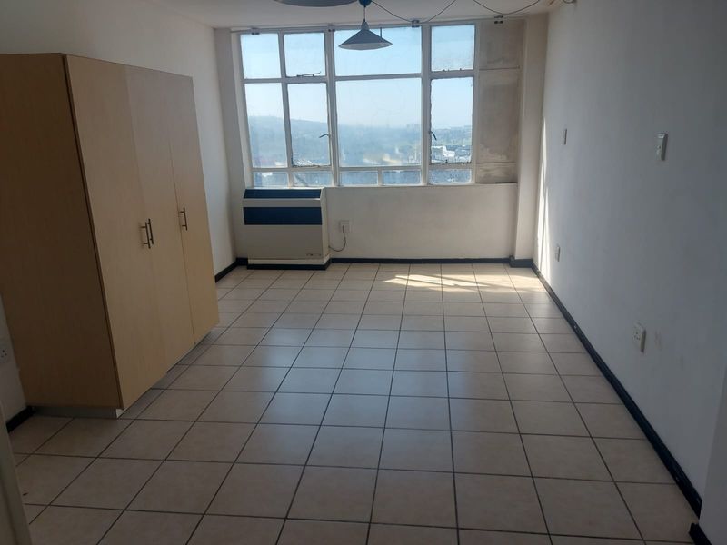A bedroom featuring tiled flooring, a large window with natural light, and a built-in air conditioning unit.