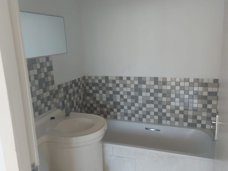 A compact bathroom featuring a pedestal basin, bathtub with tiled splashback, and tiled flooring. The space is functional but requires cosmetic updates.