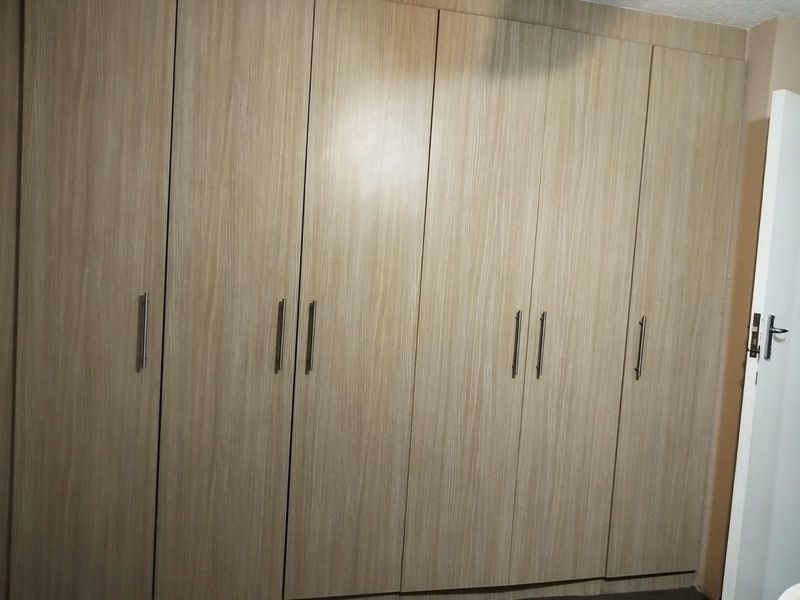 A bedroom featuring floor-to-ceiling built-in cupboards with a light wood-grain finish and modern metal handles.