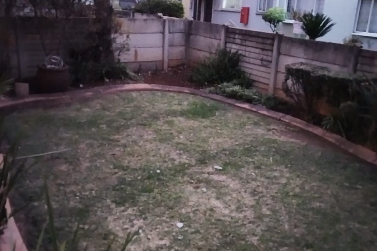 A rear garden area featuring a lawn and precast concrete boundary wall, viewed from the back of the apartment building at dusk.