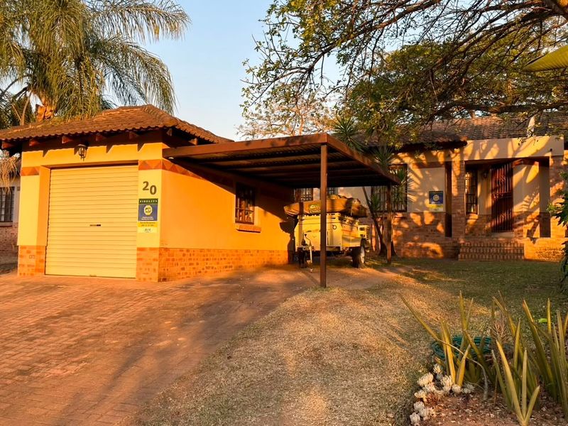 Front exterior view of the house featuring a single garage, attached carport, paved driveway, and established garden surroundings.