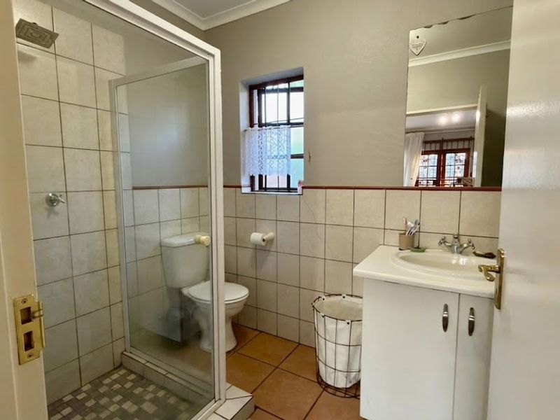 A functional bathroom featuring a shower enclosure, vanity cabinet with basin, toilet, and neutral wall and floor tiling.