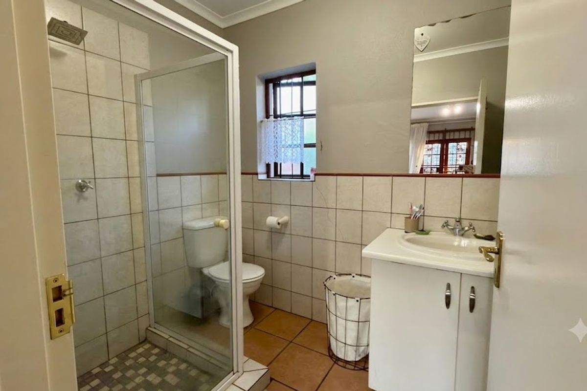 A functional bathroom featuring a shower enclosure, vanity cabinet with basin, toilet, and neutral wall and floor tiling.