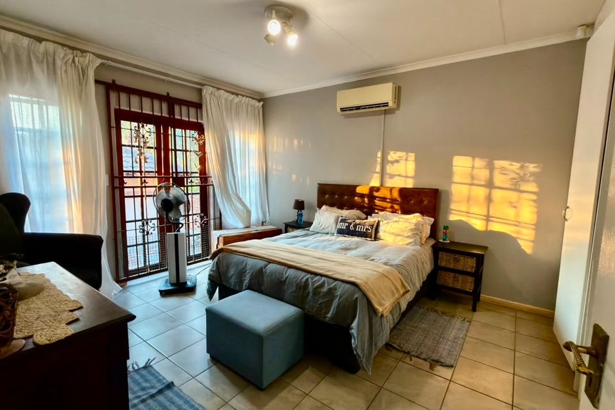 A bedroom featuring tiled flooring, a wall-mounted air conditioning unit, and a security gate leading to the exterior.