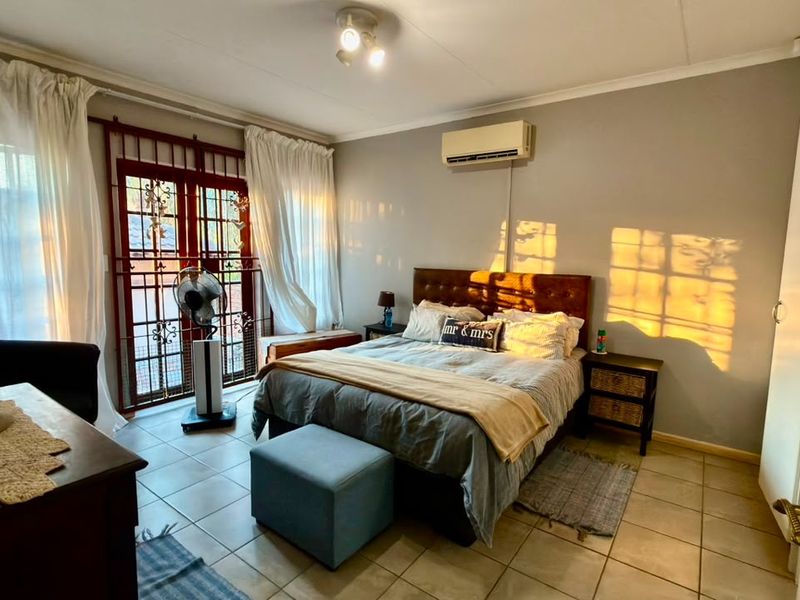 A bedroom featuring tiled flooring, a wall-mounted air conditioning unit, and a security gate leading to the exterior.