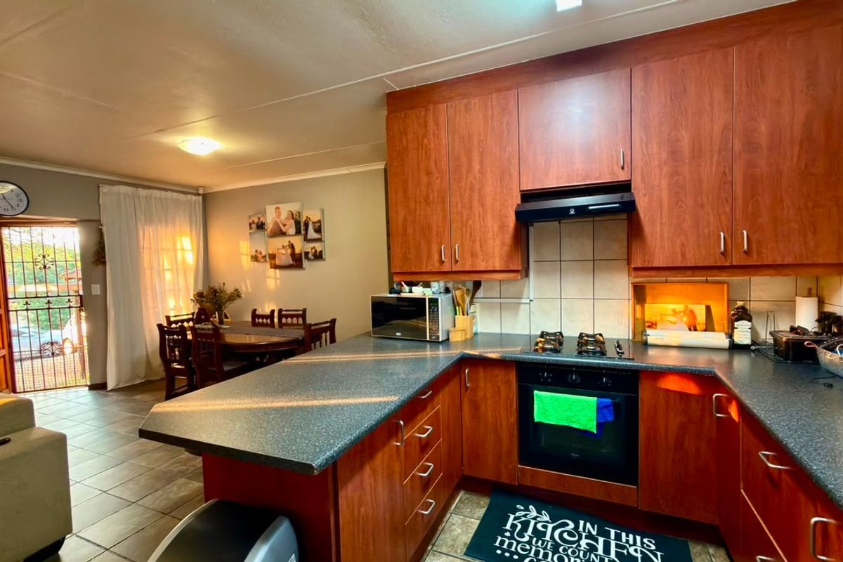Open-plan kitchen featuring cherry wood cabinetry, laminate countertops, and built-in appliances, flowing into a dining area with direct access to the exterior.