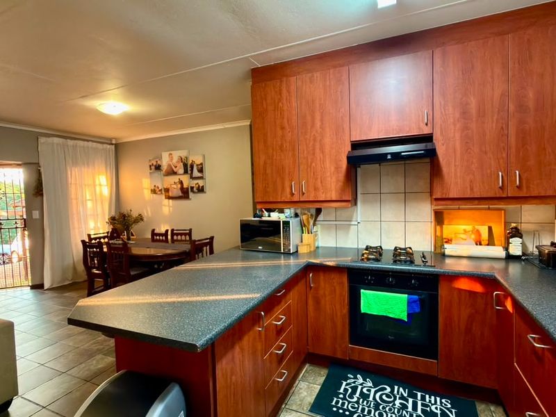 Open-plan kitchen featuring cherry wood cabinetry, laminate countertops, and built-in appliances, flowing into a dining area with direct access to the exterior.