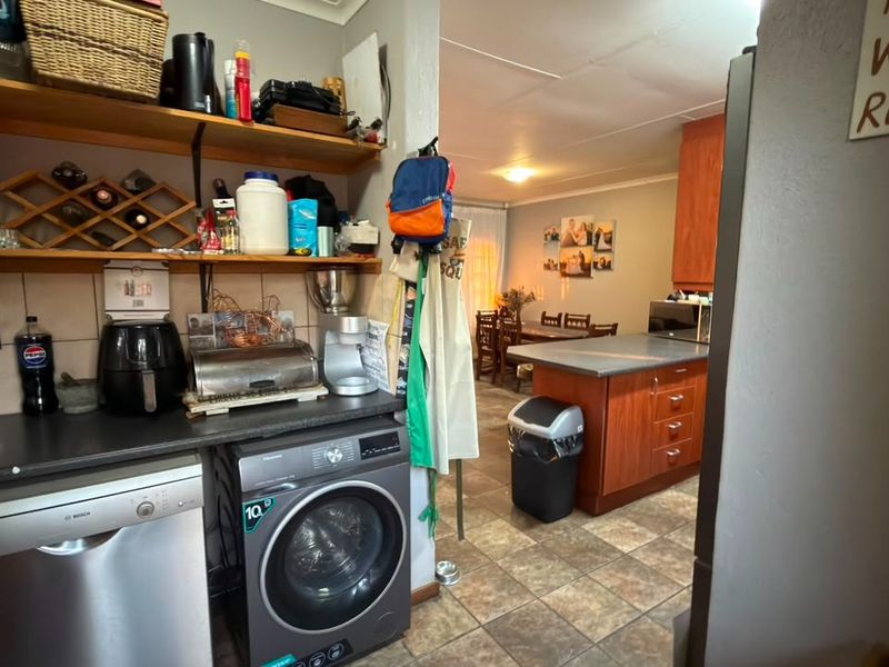 A functional scullery area featuring built-in cabinetry, laminate countertops, and tiled flooring, with direct access to the adjacent kitchen and dining space.