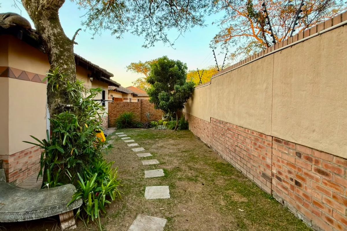 A private rear garden area featuring a brick boundary wall with electric fencing, a stone paver pathway, and established trees.