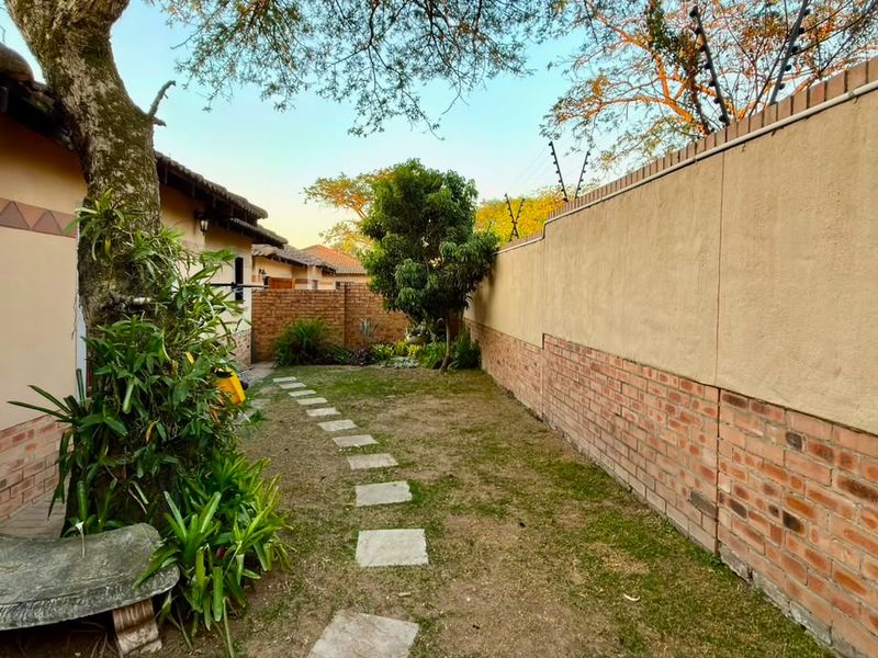 A private rear garden area featuring a brick boundary wall with electric fencing, a stone paver pathway, and established trees.