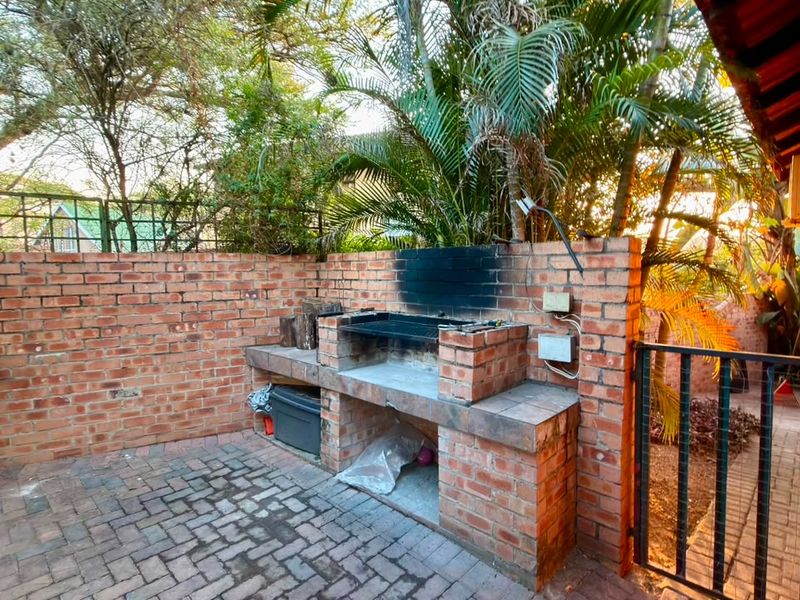 Outdoor patio area featuring a built-in brick braai, paved flooring, and a secure metal gate, set against a private garden backdrop.