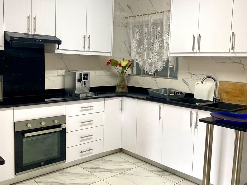 Modern kitchen featuring white cabinetry, contrasting black stone countertops, marble-look tiling, and integrated appliances including an oven and extractor fan.