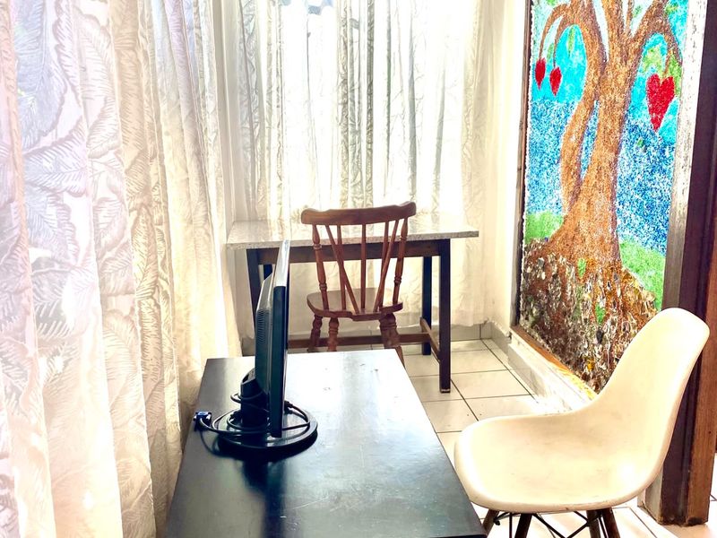A compact office space featuring tiled flooring and large windows with curtain tracks, suitable for a home workspace.