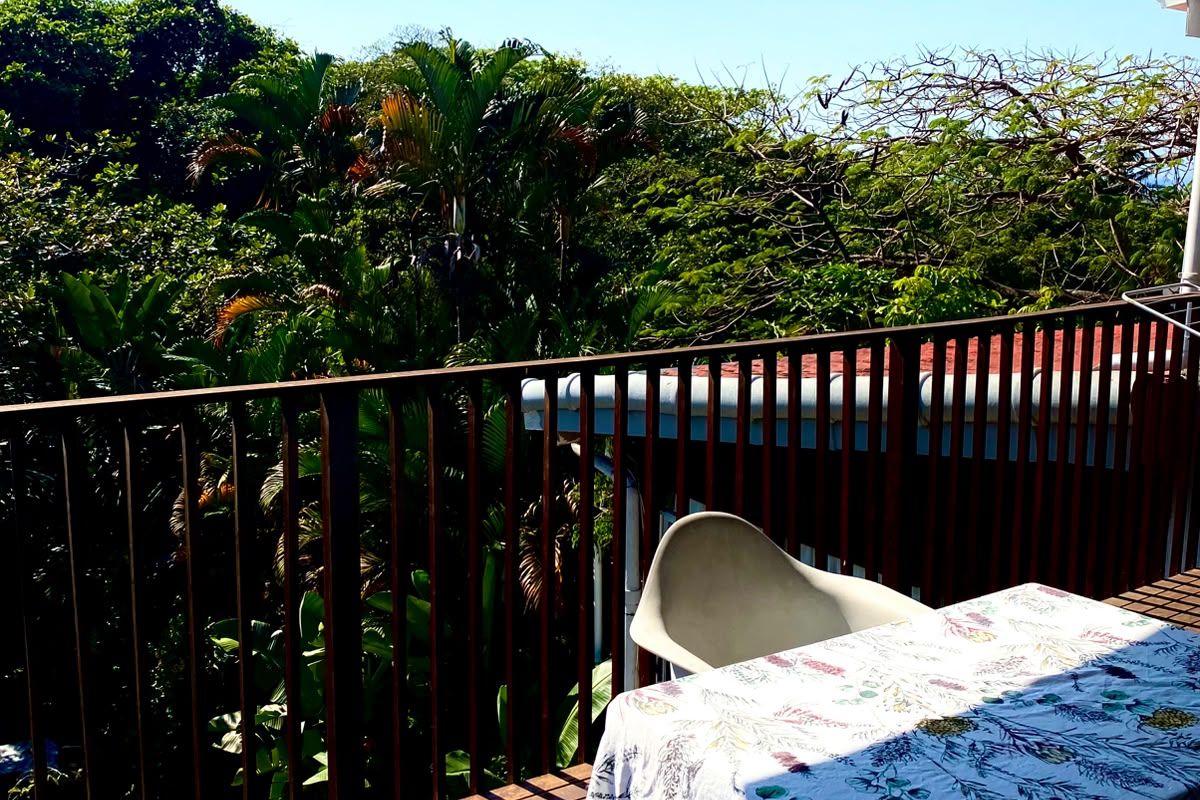 A covered balcony featuring timber decking and a metal balustrade, offering a pleasant outlook over surrounding trees.