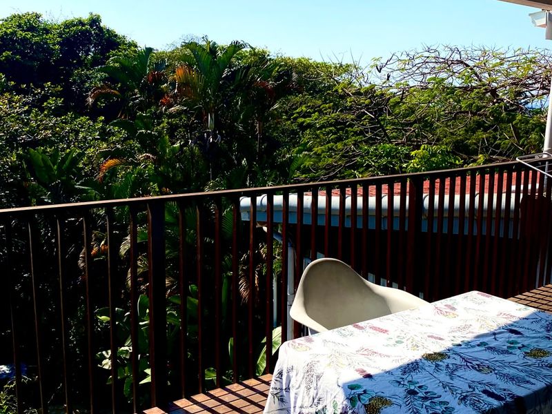 A covered balcony featuring timber decking and a metal balustrade, offering a pleasant outlook over surrounding trees.