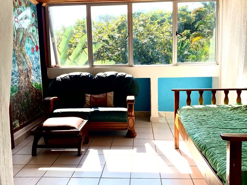 A bedroom featuring a timber-clad ceiling, ceramic tiled flooring, and large windows providing natural light and garden views.