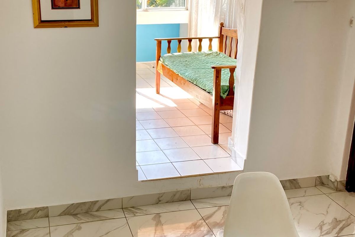 A bright living area featuring modern marble-look floor tiles and an arched doorway leading to an adjoining sunroom or balcony space.