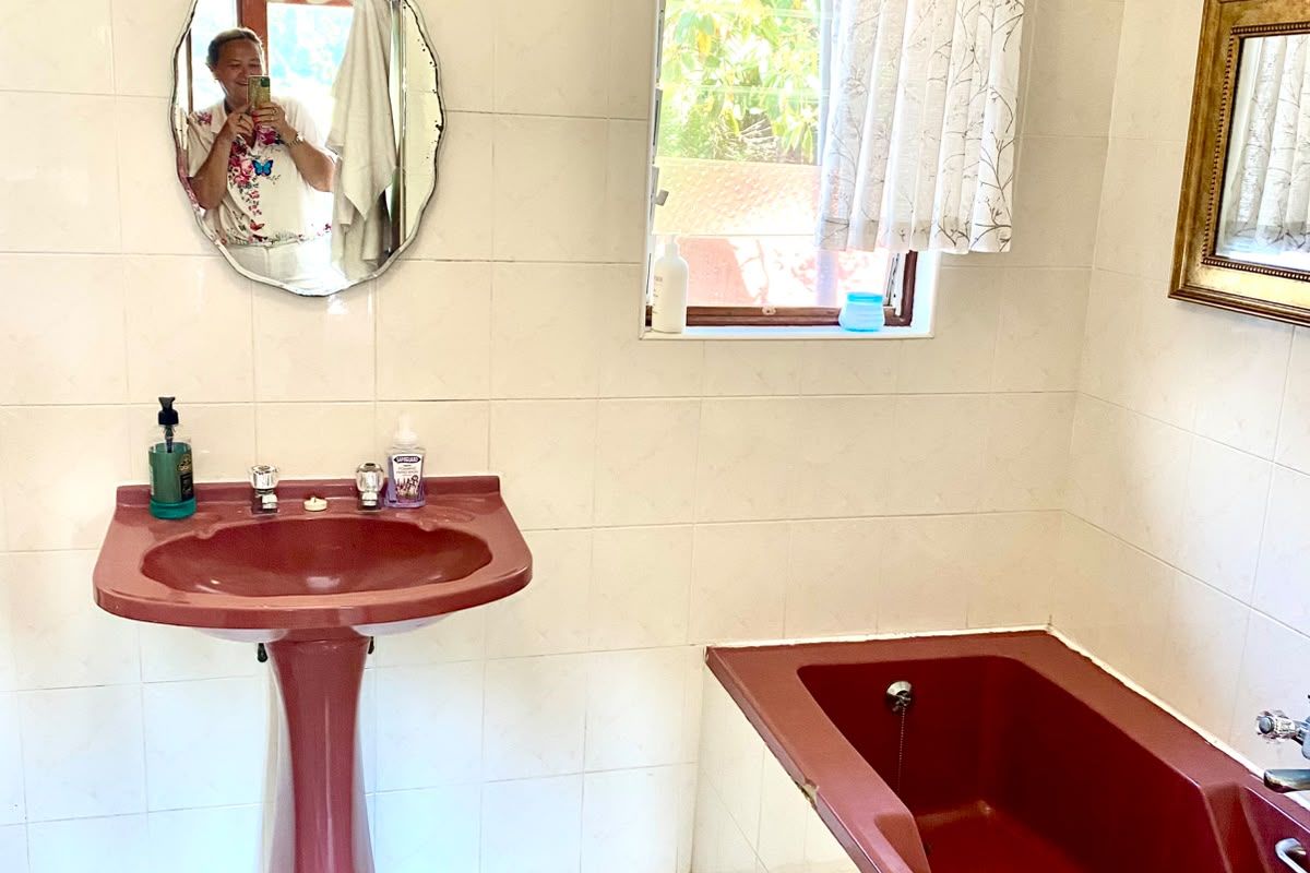 A dated bathroom featuring a burgundy pedestal basin and matching built-in bathtub, complemented by white wall and floor tiles.