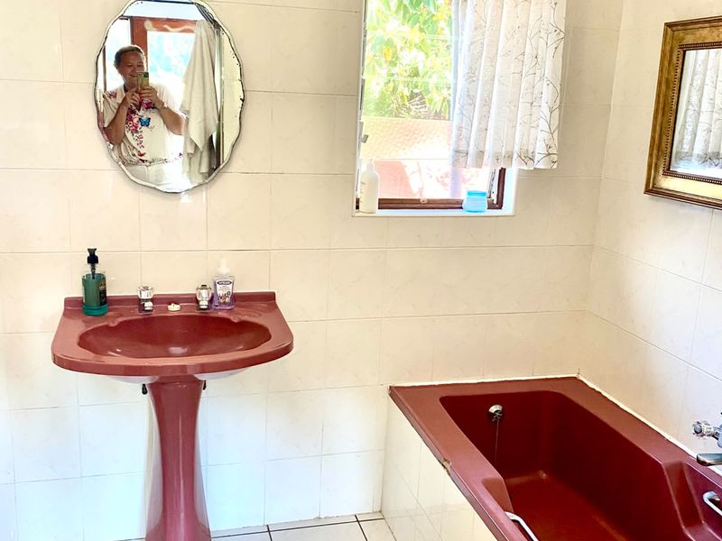 A dated bathroom featuring a burgundy pedestal basin and matching built-in bathtub, complemented by white wall and floor tiles.