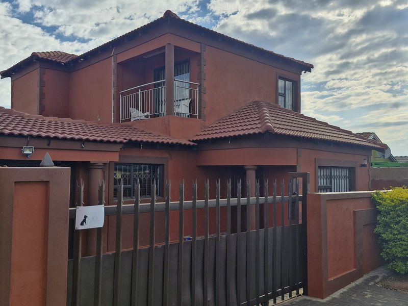 A two-story residential property featuring a tiled roof, a private balcony, and a secure gated entrance with perimeter walling.