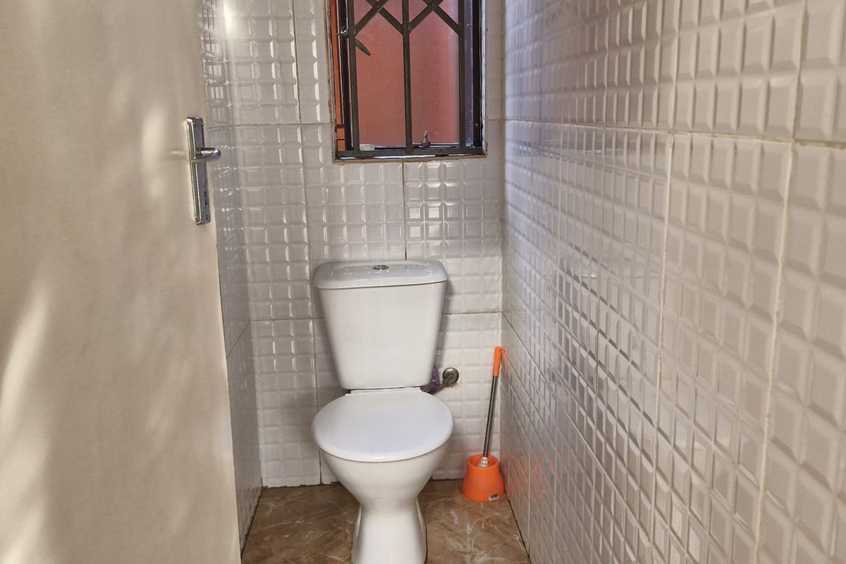 A compact bathroom featuring full-height wall tiling, tiled flooring, and a window with a security grille.