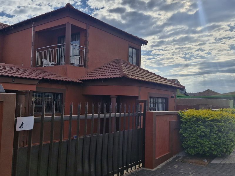 Front exterior view of a two-story house featuring a tiled roof, a private balcony, and a secure metal gate with perimeter walling.