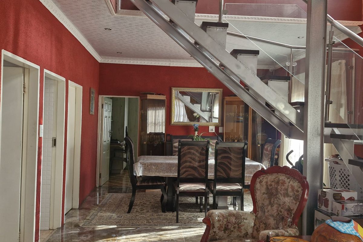 Open-plan living and dining area featuring a modern metal staircase with glass balustrades and polished tiled flooring.
