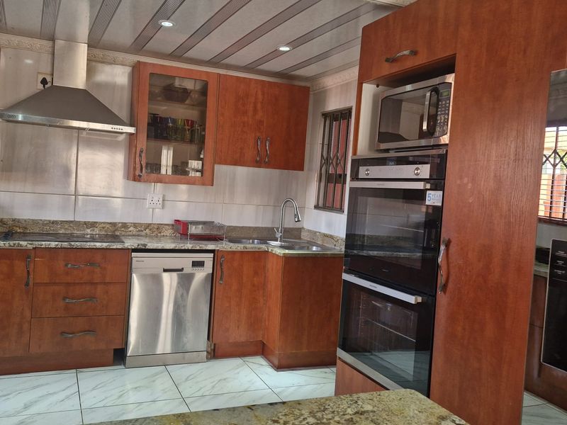 A functional kitchen featuring wooden cabinetry, granite countertops, built-in oven and microwave, stainless steel extractor fan, and tiled flooring.