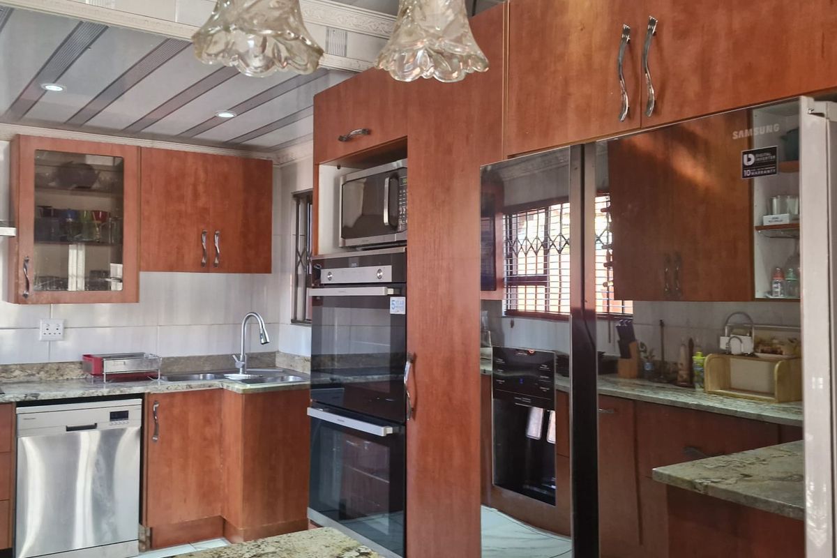 A functional kitchen featuring wooden cabinetry, granite countertops, built-in oven and microwave, and tiled flooring with modern pendant lighting.