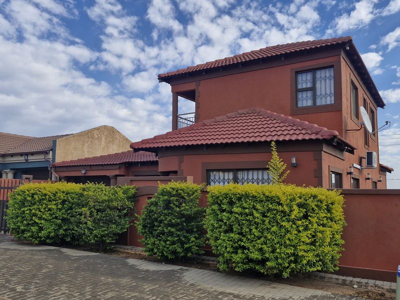 A double-storey residential property featuring a tiled roof, balcony, and secure boundary wall with a paved driveway approach.
