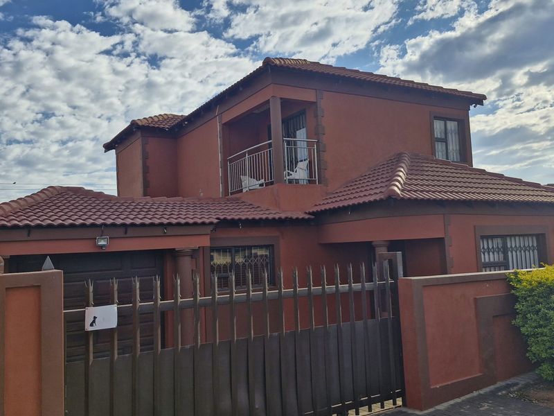 A two-story residential house featuring a terracotta-colored facade, tiled roof, secure metal gate, and an upper-level balcony.