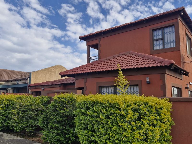 Front elevation of a two-story residential house featuring terracotta roof tiles, a brick boundary wall, and established garden hedging.