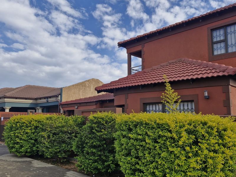 A view of the front facade of a two-story house featuring terracotta roof tiles, paved driveway, and established garden hedging.