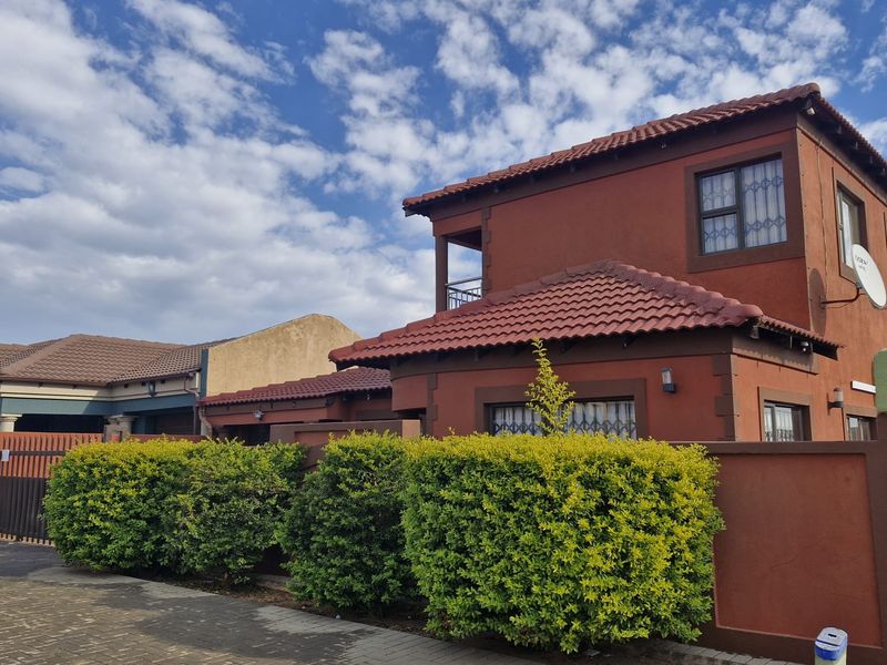 A well-maintained two-story residential property featuring a terracotta tiled roof, a private balcony, and a secure boundary wall with a paved driveway.