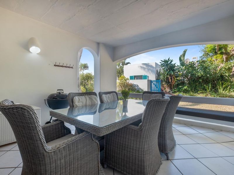 A covered patio area featuring tiled flooring, a built-in bench, and an arched opening leading to the garden.