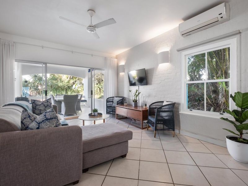 Bright living room featuring tiled flooring, a ceiling fan, split-system air conditioning, and large sliding doors providing seamless access to the outdoor patio area.