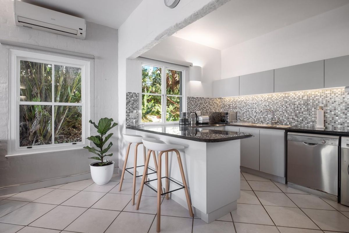 Modern kitchen featuring granite countertops, mosaic tile backsplash, sleek cabinetry, and a breakfast bar, complemented by natural light and split-system air conditioning.